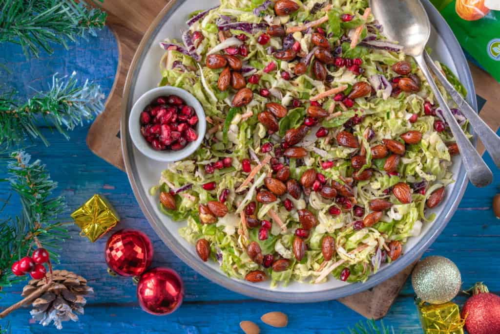 Healthy Brussels sprout slaw that comes with a creamy tahini dressing, spicy roasted almonds and pomegranates for a bit of sweetness. It's naturally vegan and gluten-free too! #veganchristmas #brusselssprouts #veganchristmas #christmasfood #healthychristmas #christmasfood #plantbased