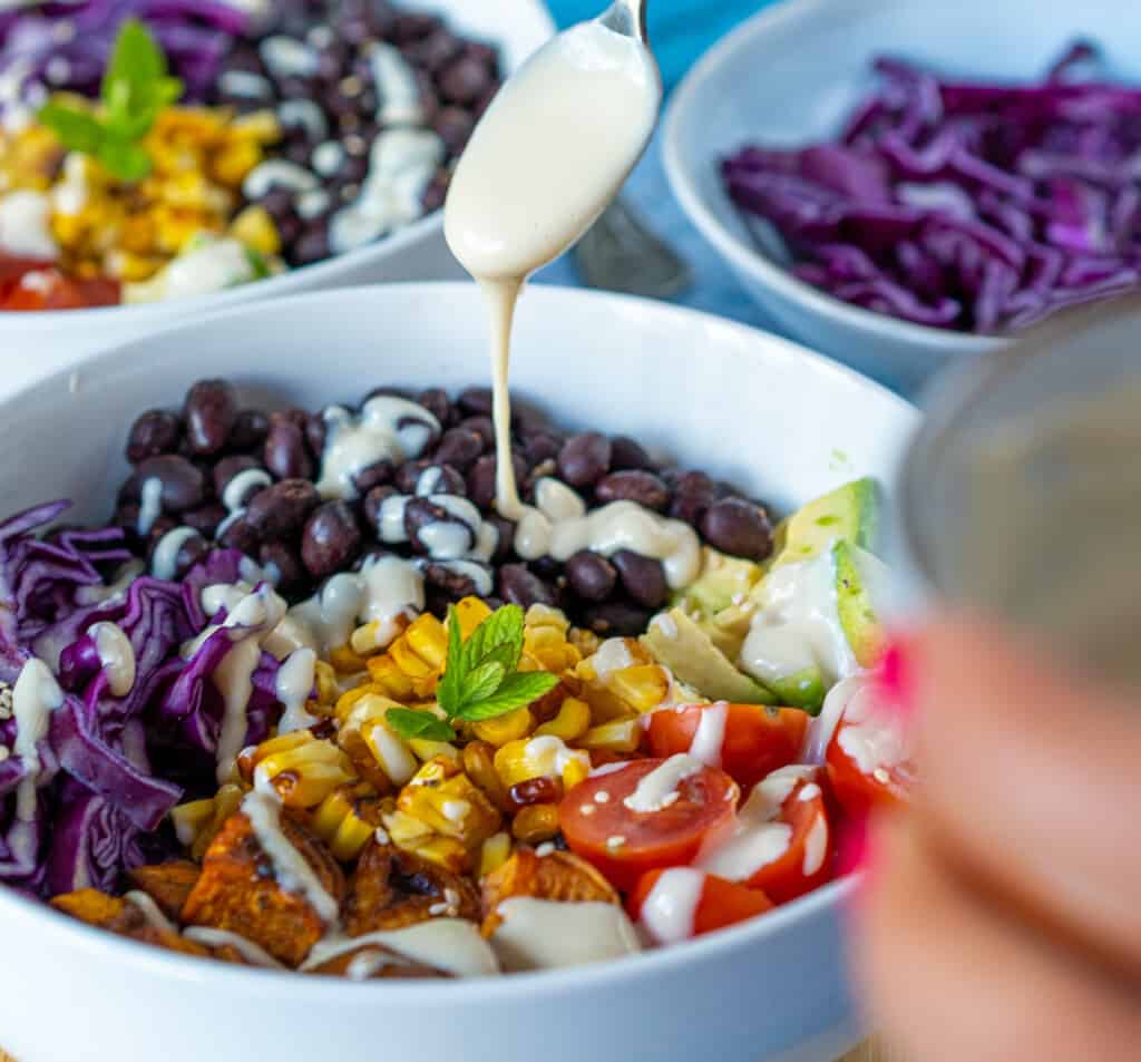 The best healthy Burrito Buddha Bowl packed with roasted sweet potatoes, smokey black beans, cherry tomatoes , creamy avocado and sweetcorn all drizzled with lush yoghurt and tahini dressing.